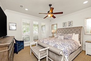 A bedroom with a bed, a ceiling fan, a desk, a chair, and a window with blinds.