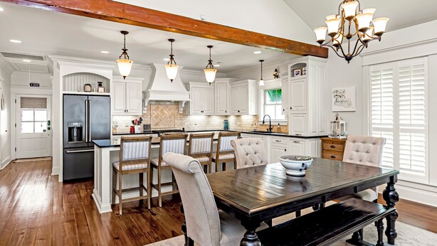 A spacious kitchen with white cabinetry, a central island, and a dining area with a dark wooden table and chairs.
