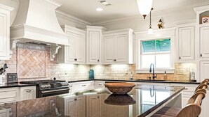A modern kitchen with white cabinets, a large island, and a herringbone-patterned backsplash.