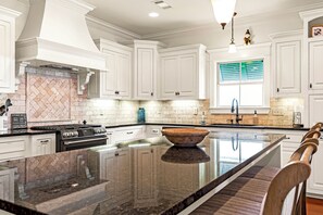 A modern kitchen with white cabinets, a large island, and a herringbone-patterned backsplash.