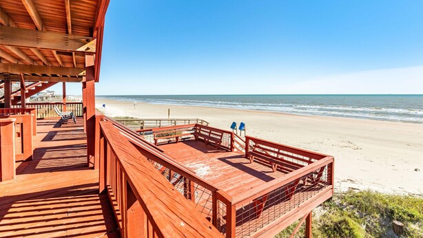 Eine Holzterrasse mit Blick auf Strand und Meer.