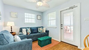 Ein Wohnzimmer mit einer Couch, einem Hocker, einem Deckenventilator und zwei Fenstern mit Jalousien.