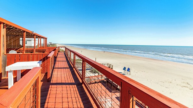 A wooden deck with a railing overlooking a beach.