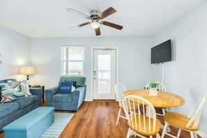 A living room with a ceiling fan, a dining table with chairs, a sofa, a bench, a TV mounted on the wall, and a door with a window.