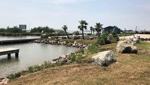 A lakeside park with a wooden dock, large rocks, and palm trees.