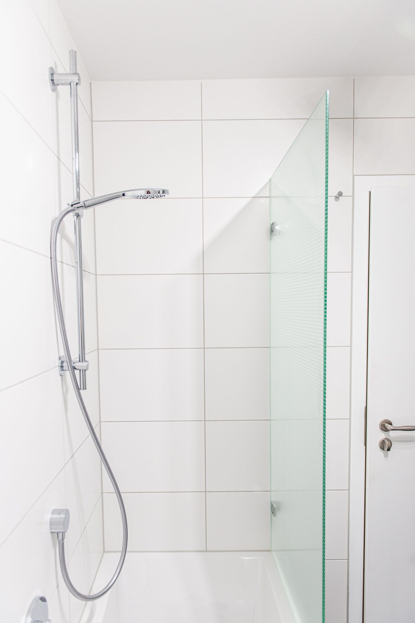 Une douche moderne dotée d’une porte en verre et d’un pommeau de douche chromé.