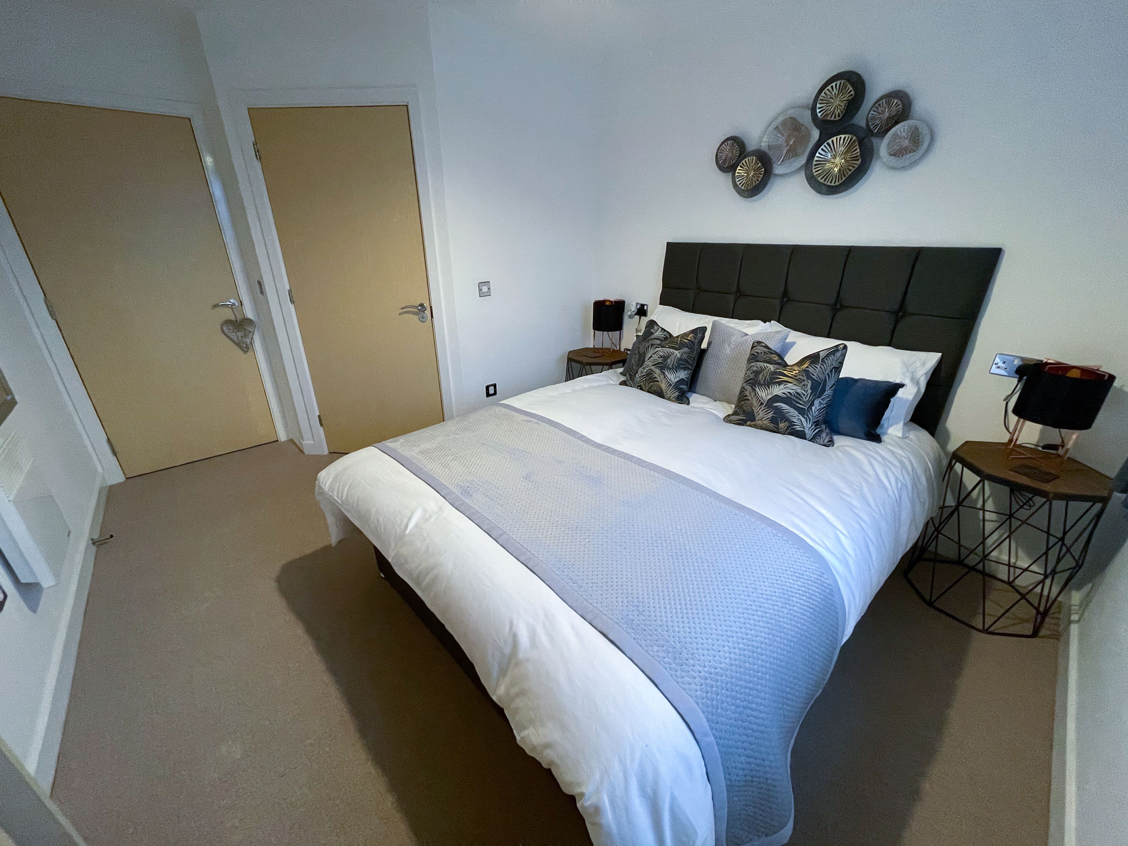 A neatly arranged bedroom with a large bed, a headboard, and a wall-mounted decorative piece.
