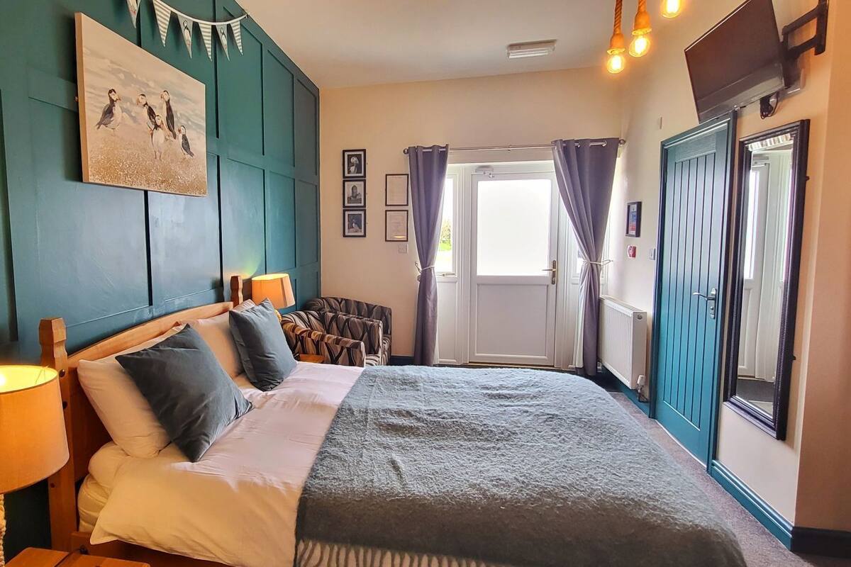 A bedroom with a bed, bedside lamps, a window with curtains, a door, and a wall with a picture.