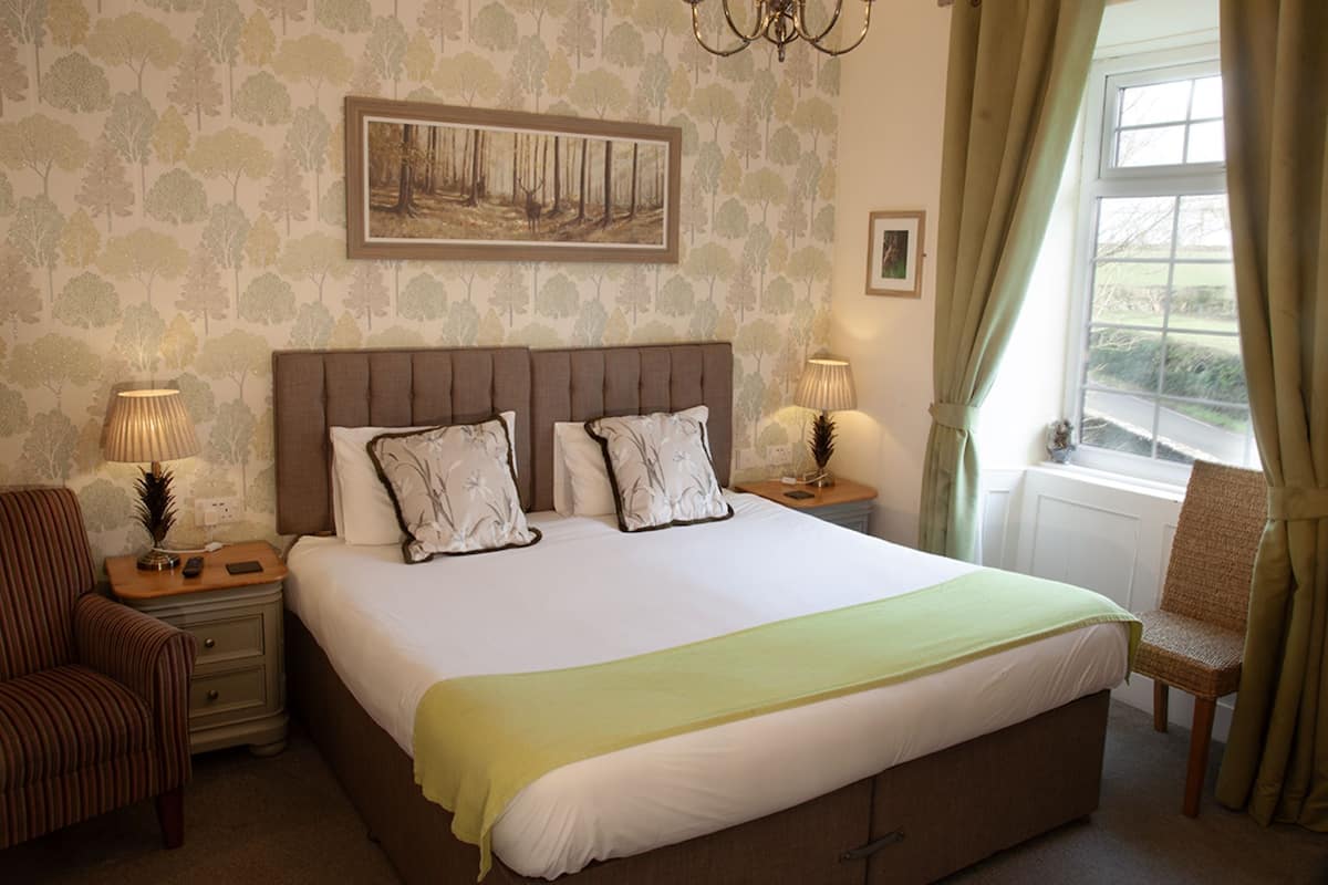 A neatly arranged bedroom with a large bed, two bedside tables, a chair, and a window with curtains.