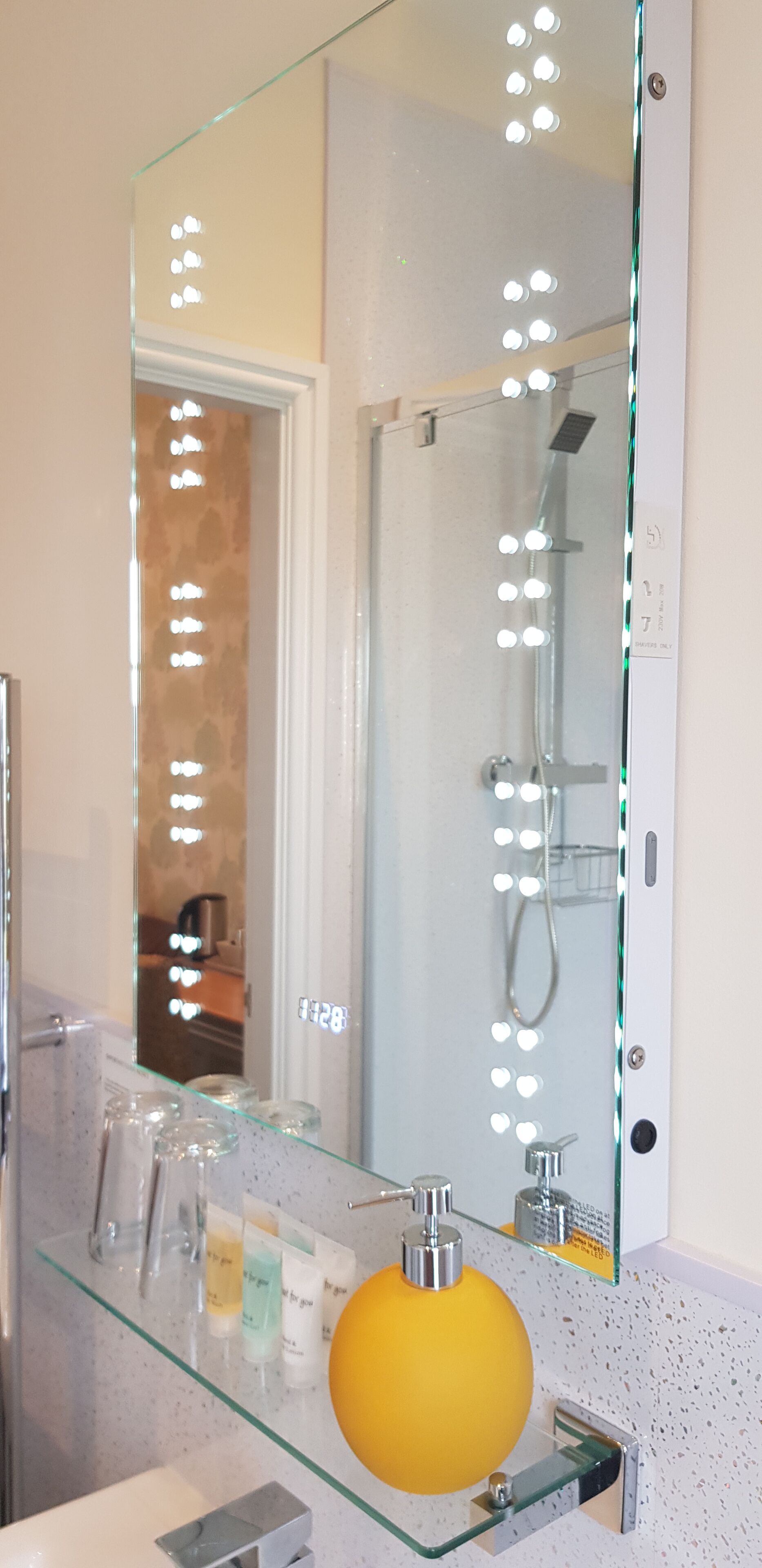 A bathroom with a glass vanity, a yellow soap dispenser, and a mirror with lights.