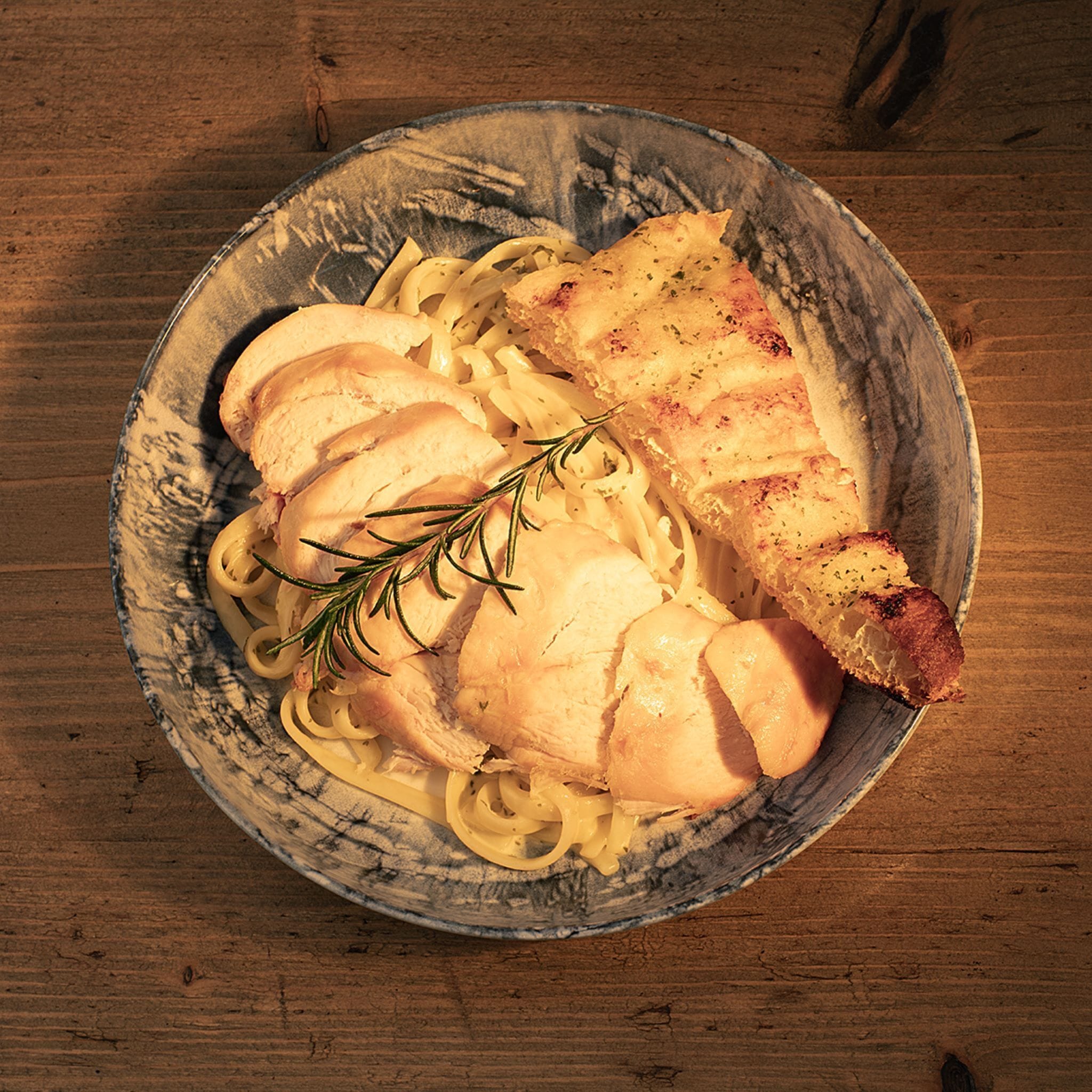 A plate of chicken and pasta on a rustic wooden table.