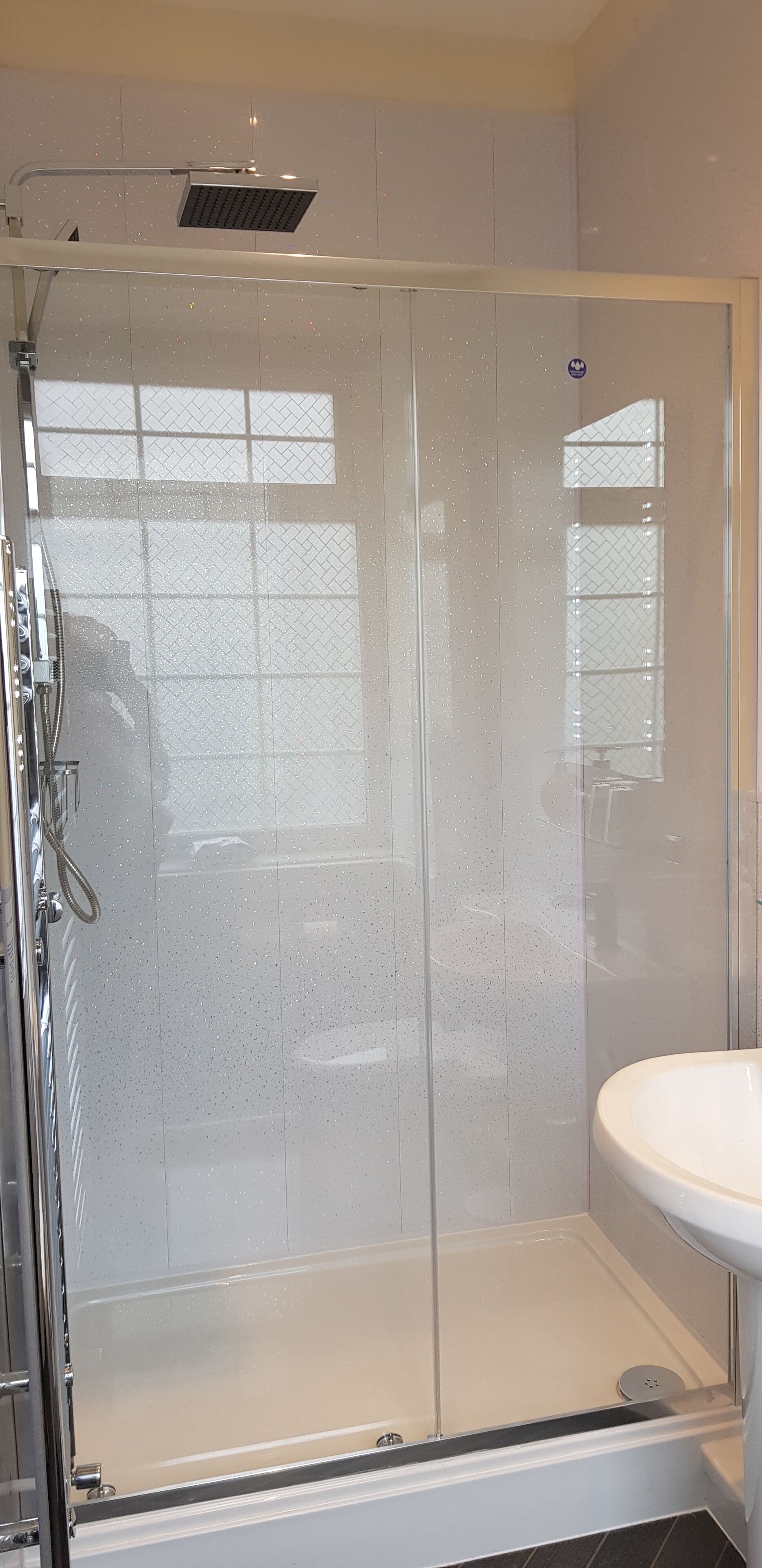 Eine begehbare Dusche mit Glasabtrennung und ein weißes Waschbecken zur Rechten.