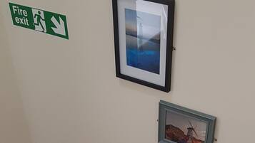 A staircase with a white railing, a fire exit sign, and three framed pictures on the wall.