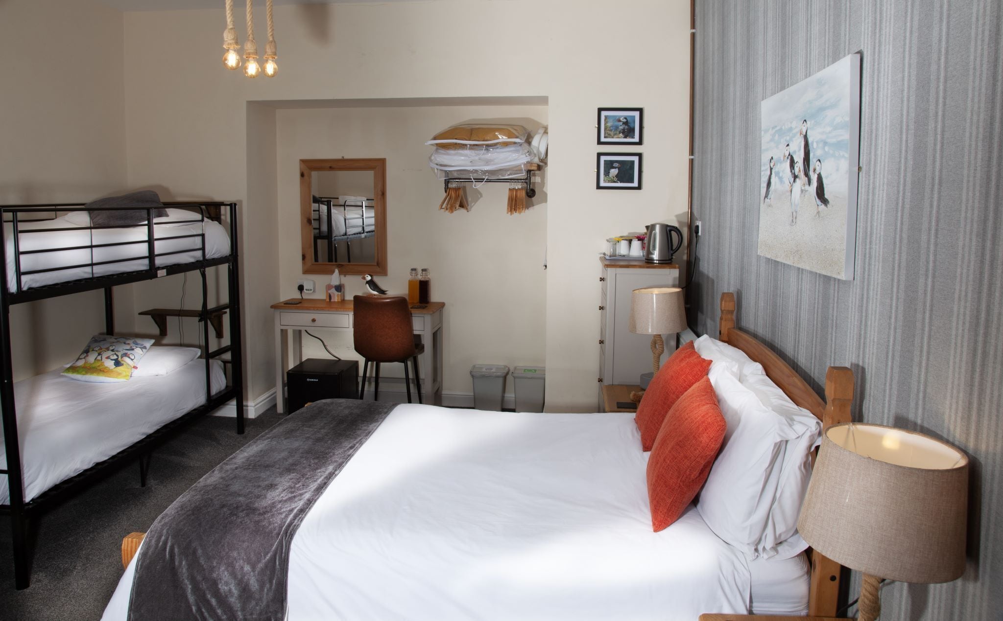 Een hotelkamer met stapelbedden, een bureau, een stoel, een lamp en een ingelijst schilderij aan de muur.