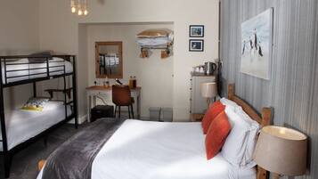 A hotel room with bunk beds, a desk, a chair, a lamp, and a framed picture on the wall.