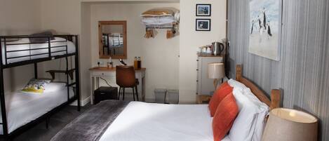 Een hotelkamer met stapelbedden, een bureau, een stoel, een lamp en een ingelijst schilderij aan de muur.