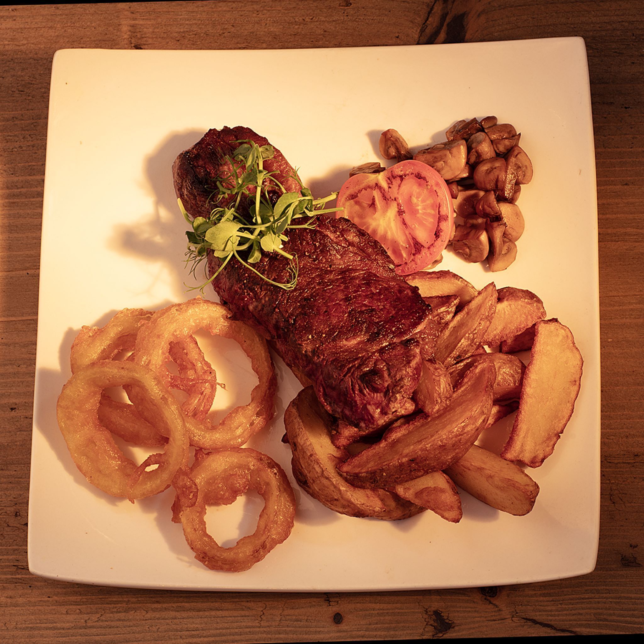 A plate with a steak, mushrooms, and onion rings.