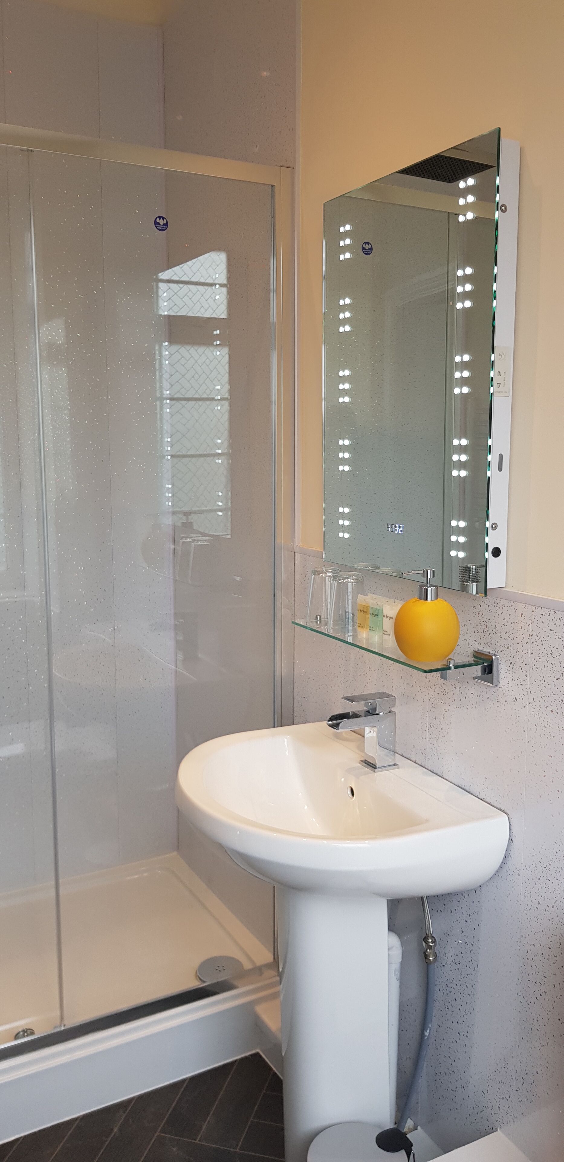 Un baño moderno con cabina de ducha de vidrio, un lavamanos blanco con grifo cromado y un espejo con iluminación.