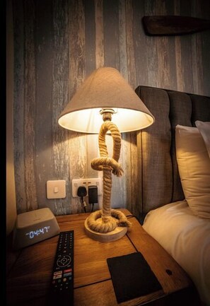 A wooden nightstand with a lamp, a remote control, and a digital clock displaying 04:47. - The Ring Pub Bed and Breakfast (Rhosgoch)