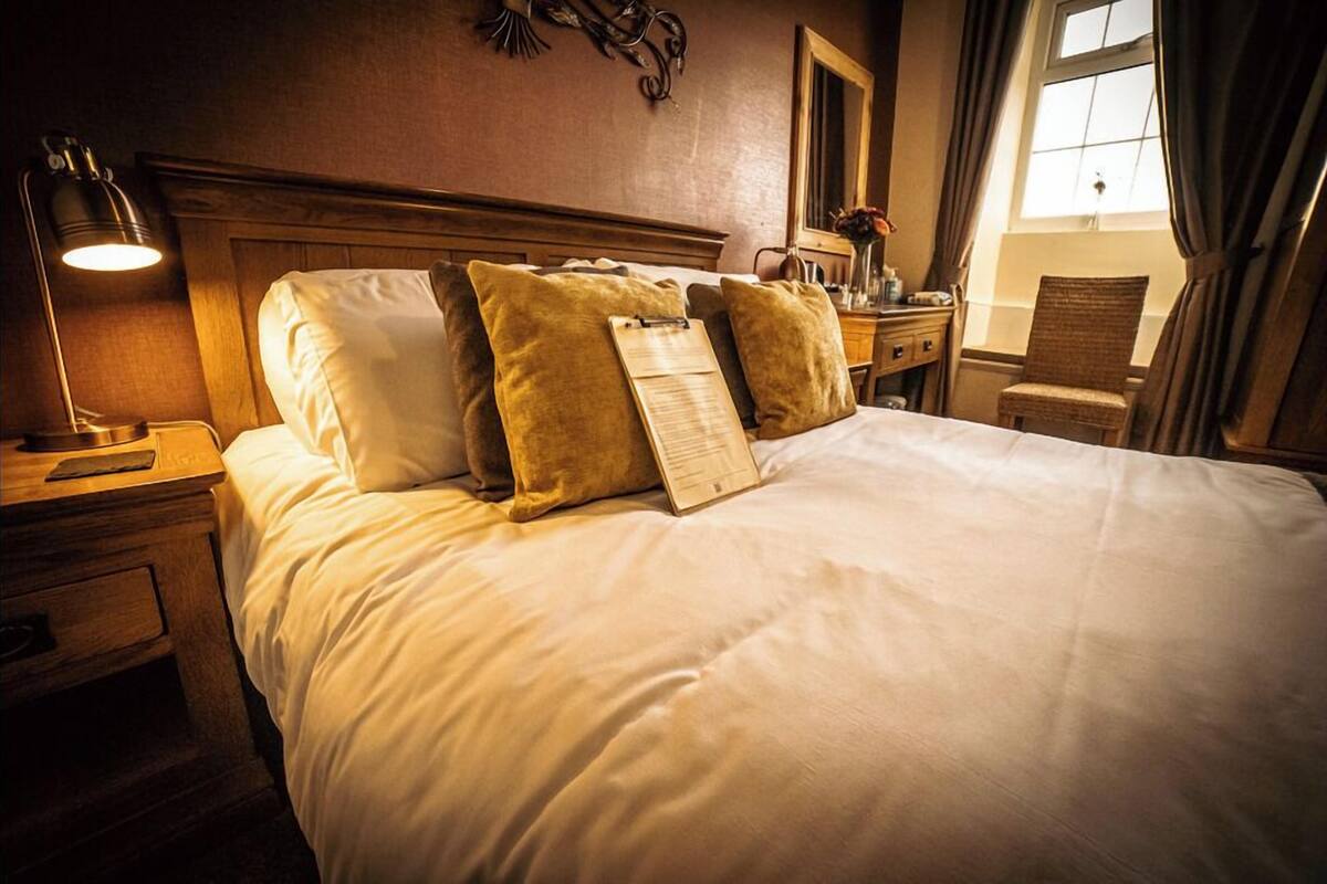 A neatly made bed with a headboard, a bedside lamp, a nightstand, and a chair.