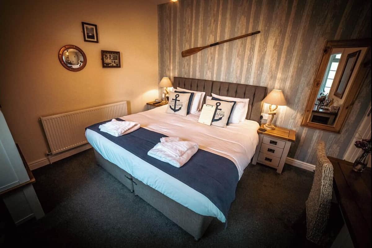 A neatly made bed with pillows, a bedside table with a lamp, a mirror, and a wooden wall with a hanging bat.