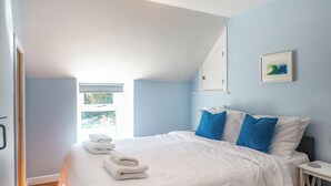 Ein Schlafzimmer mit einem Bett, Kissen, einem Nachttisch, einem Fenster und einem Wandbild.