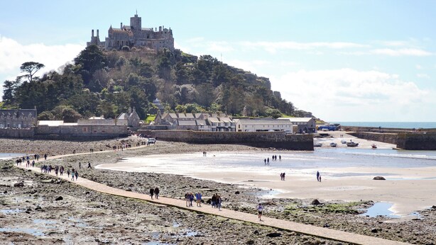 Eine Küstenstadt mit einer markanten Burg auf einem Hügel, einem Sandstrand und einer Uferpromenade.