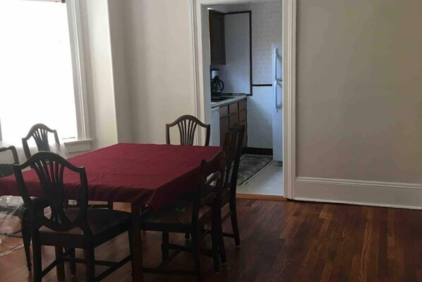 Ein Essbereich mit einem roten Tisch und vier Stühlen, der in eine Küche mit Schränken und einem Kühlschrank übergeht.