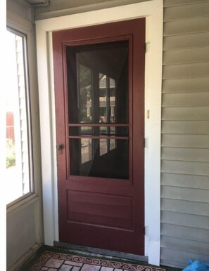 Puerta roja con un panel de vidrio y una sección decorativa en la parte inferior.