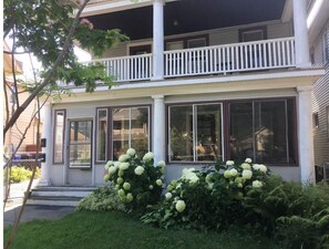 Ein zweistöckiges Haus mit Veranda, großen Fenstern und einem weißen Zaun.