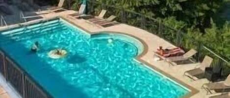 Una piscina rectangular con borde curvo, rodeada de sillas de descanso y una pequeña terraza.