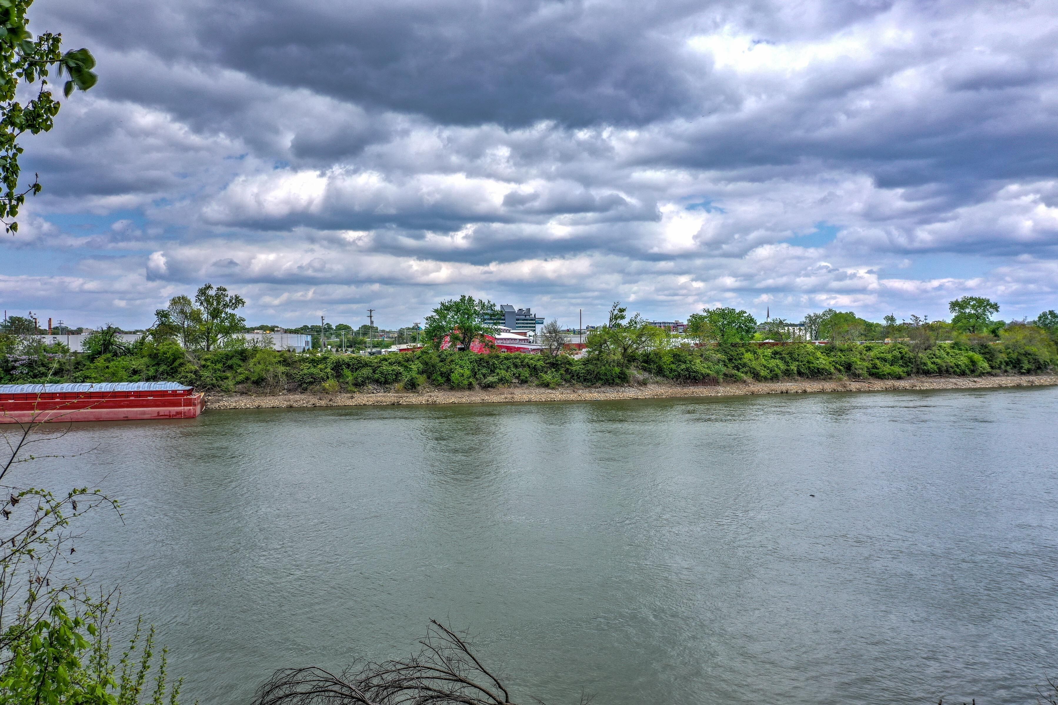 A river with a red boat docked on the left, surrounded by greenery and buildings in the background.