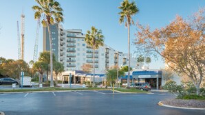Un hotel dal design moderno, con ingresso coperto, diversi piani e un'area parcheggio con alcune auto.