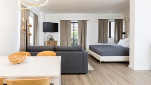 Un soggiorno moderno e luminoso con divano, tavolo da pranzo con sedie, televisore a schermo piatto e un letto con testiera.