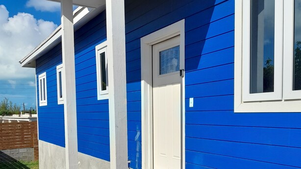 Ein blaues Haus mit weißer Tür und Fenstern, einer Veranda mit Stufen und einem Schotterweg.