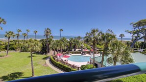 A pool area with a view of the ocean, surrounded by palm trees and a fenced deck with lounge chairs. - Fabulous ocean view from every room in this top floor villa in Palmetto Dunes (Hilton Head Island)