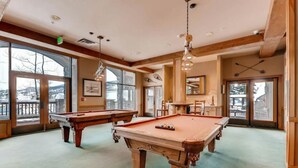 Une salle de billard avec deux tables de billard, de grandes fenêtres et des poutres en bois.