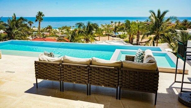 Área de piscina com vista para o oceano, cadeiras de descanso e céu azul.