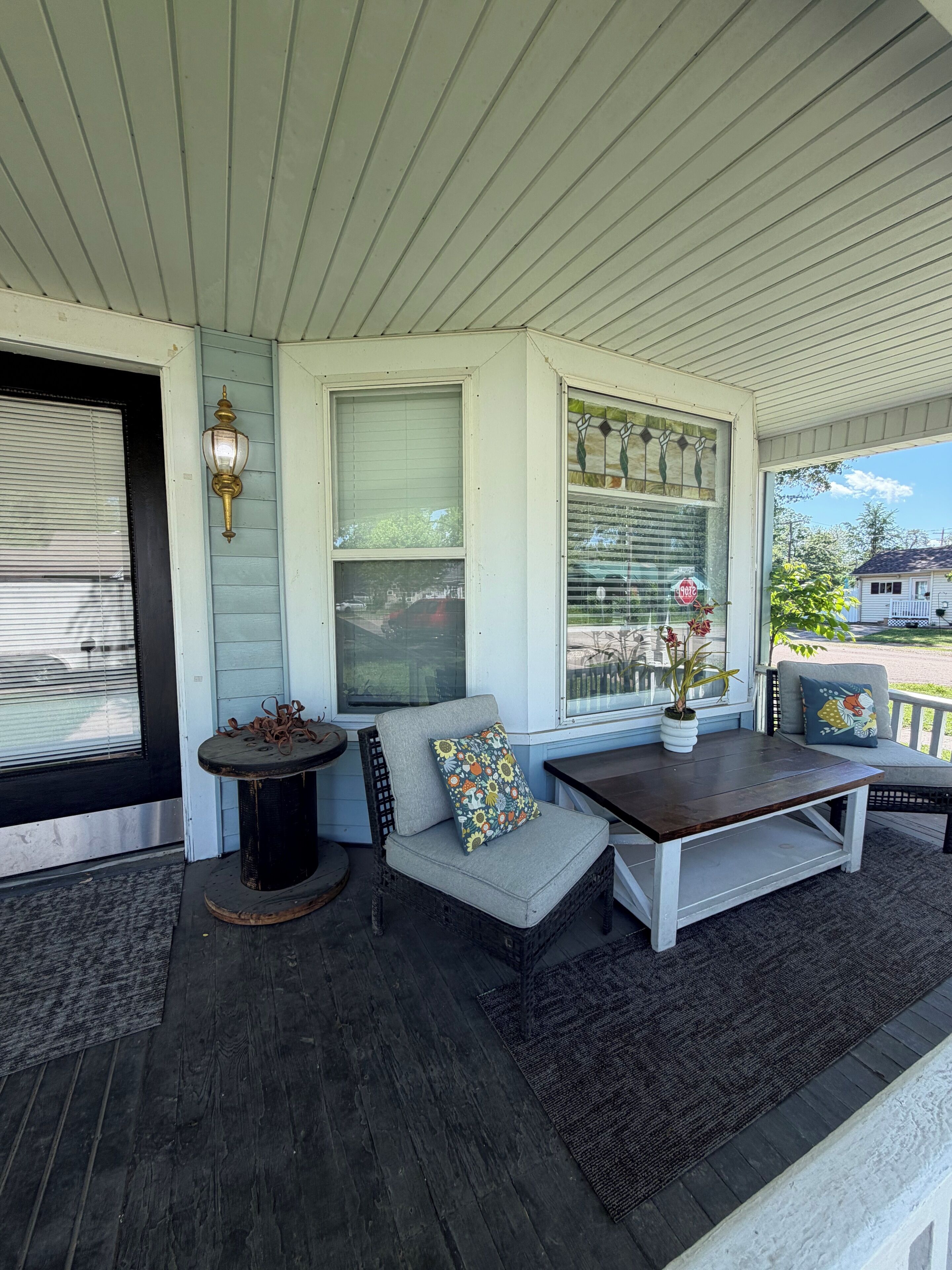 A covered porch with a seating area, a small table, a potted plant, and a decorative light fixture.