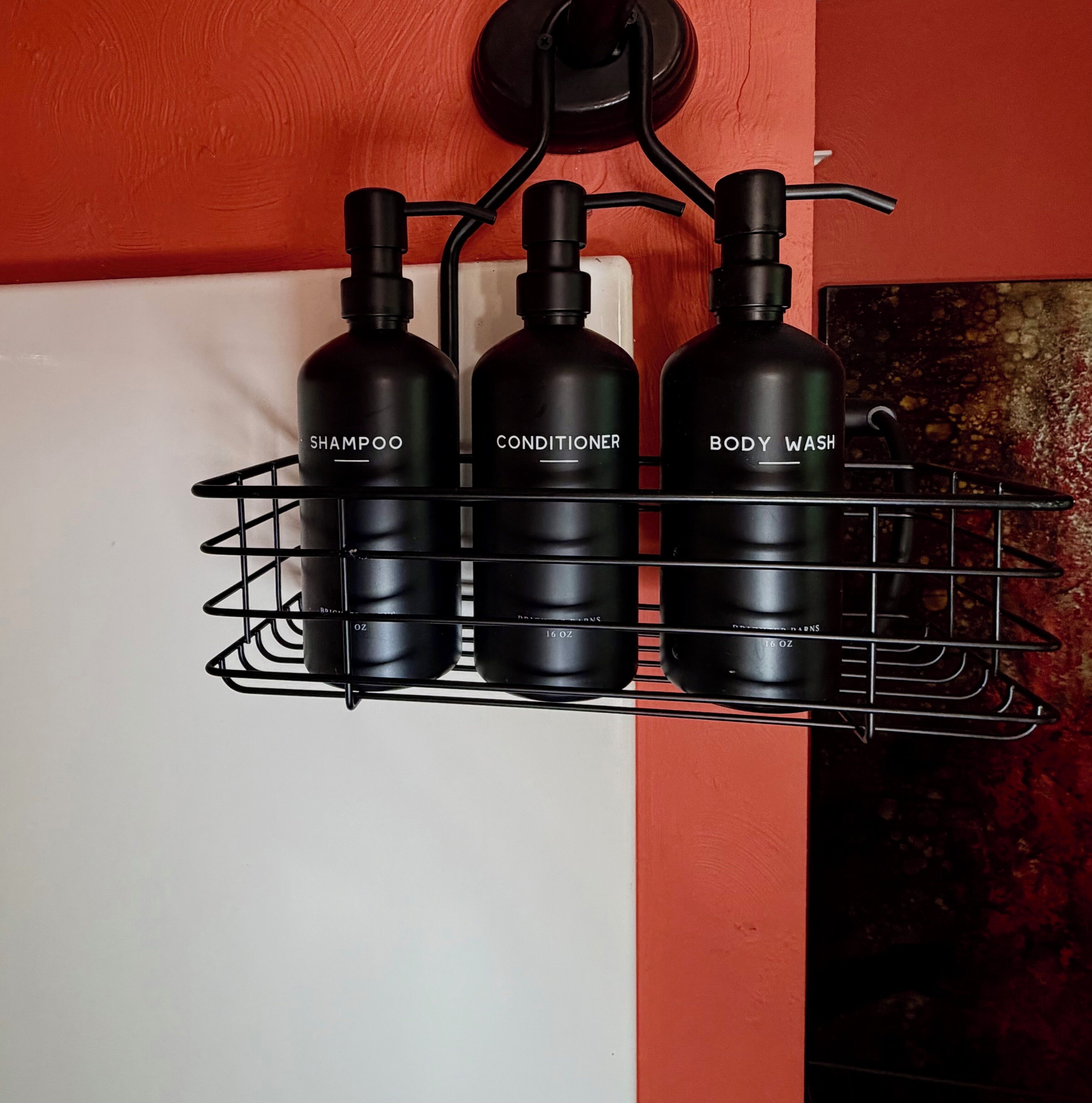 En sort metalhylde med tre flasker mærket 'SHAMPOO', 'CONDITIONER' og 'BODY WASH'.