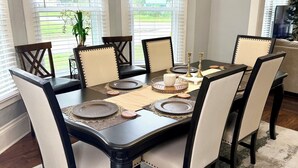 A dining area with a rectangular table, six chairs, a chandelier, and large windows. - Dexter Victorian Homestead- Brand NEW Remodel April 2026. VERY Clean & Cozy (Dexter)