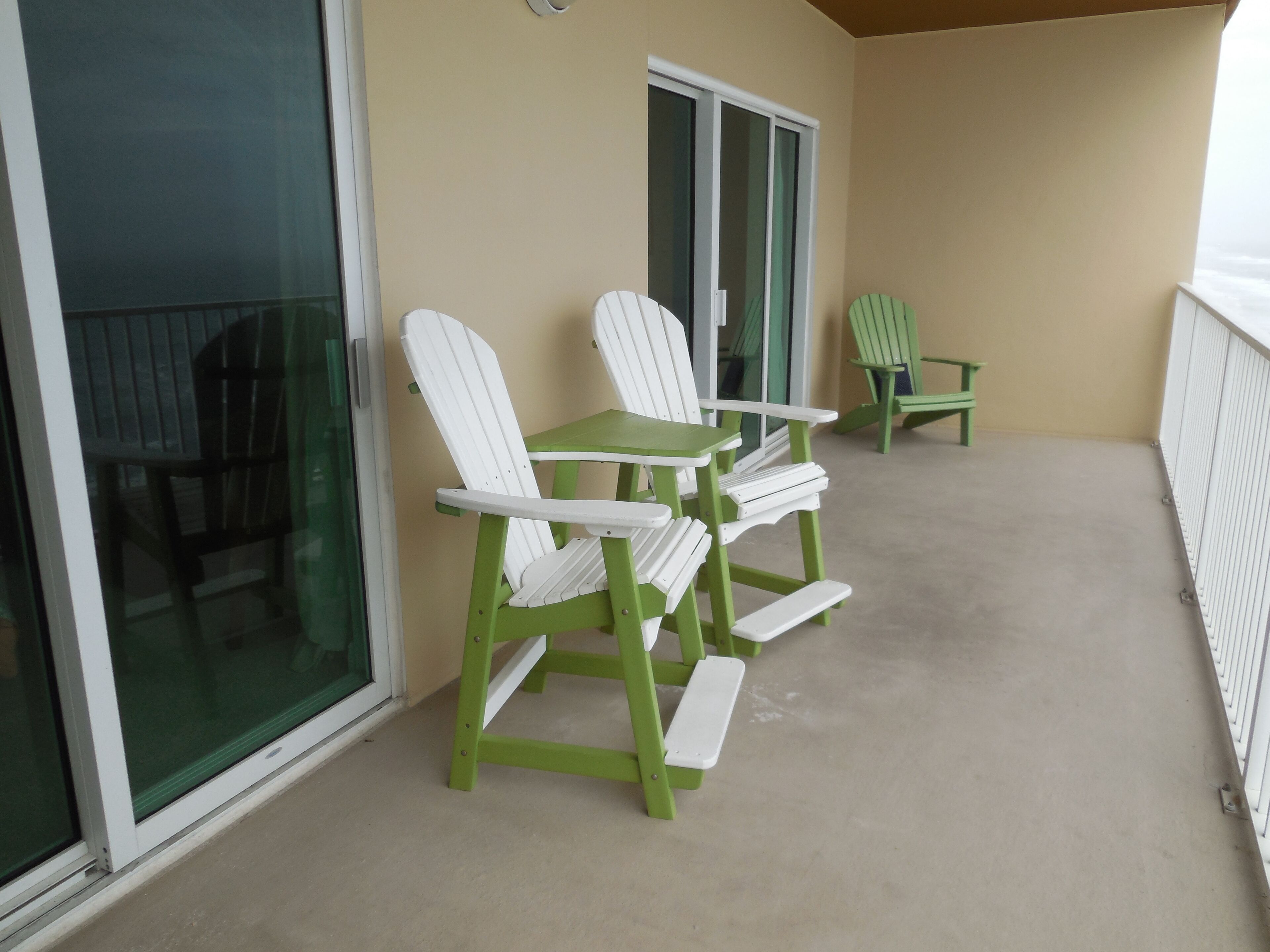 A balcony with green Adirondack chairs and a small table.