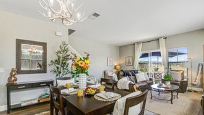 A dining area with a wooden table, chairs, and a vase of flowers. There is a sofa and a coffee table in the background.
