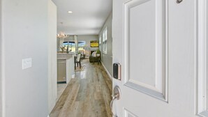 A hallway with a door, a light switch, and a view into a dining area with a table and chairs.