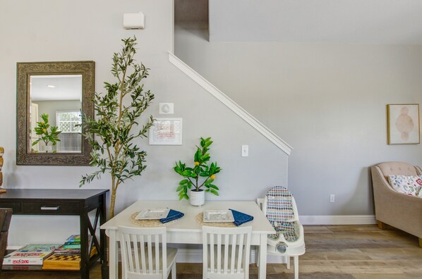 Un coin repas avec une table et des chaises blanches, une petite plante en pot et un miroir au mur.