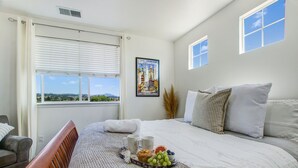 A bedroom with a bed, a bedside table with a tray of breakfast, a window with blinds, and a poster on the wall.