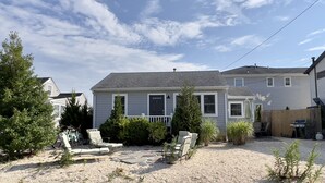 A two-story house with a front porch, a gravel driveway, and a backyard with a patio and outdoor furniture. - Comfy, Remodeled Beach House with Vintage Jersey Shore Charm (Lavallette)