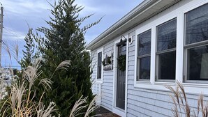 A white house with a dark front door, a small porch, and a window with a wreath. - Comfy, Remodeled Beach House with Vintage Jersey Shore Charm (Lavallette)