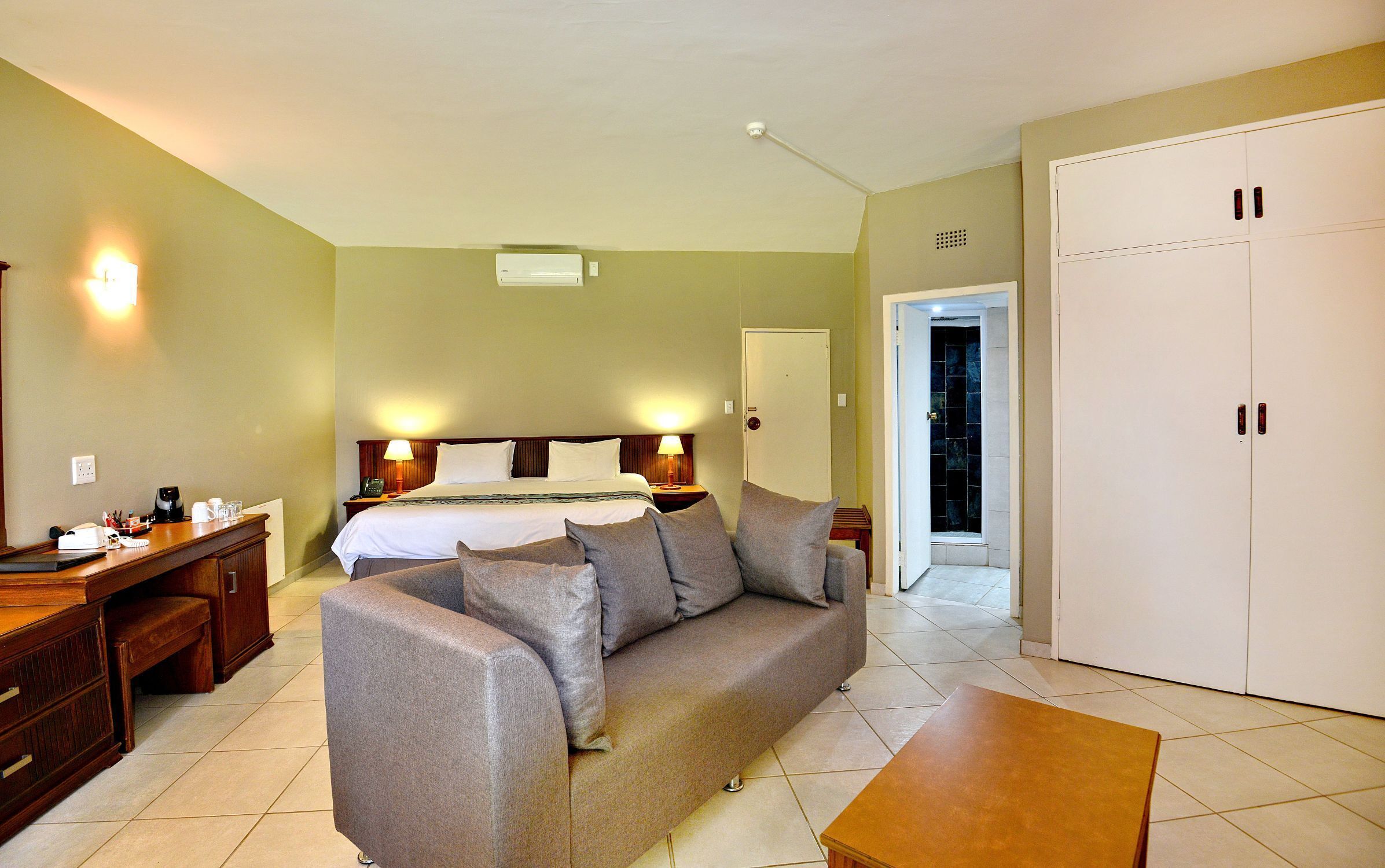 Quarto de hotel com cama, sofá, escrivaninha e guarda-roupa.
