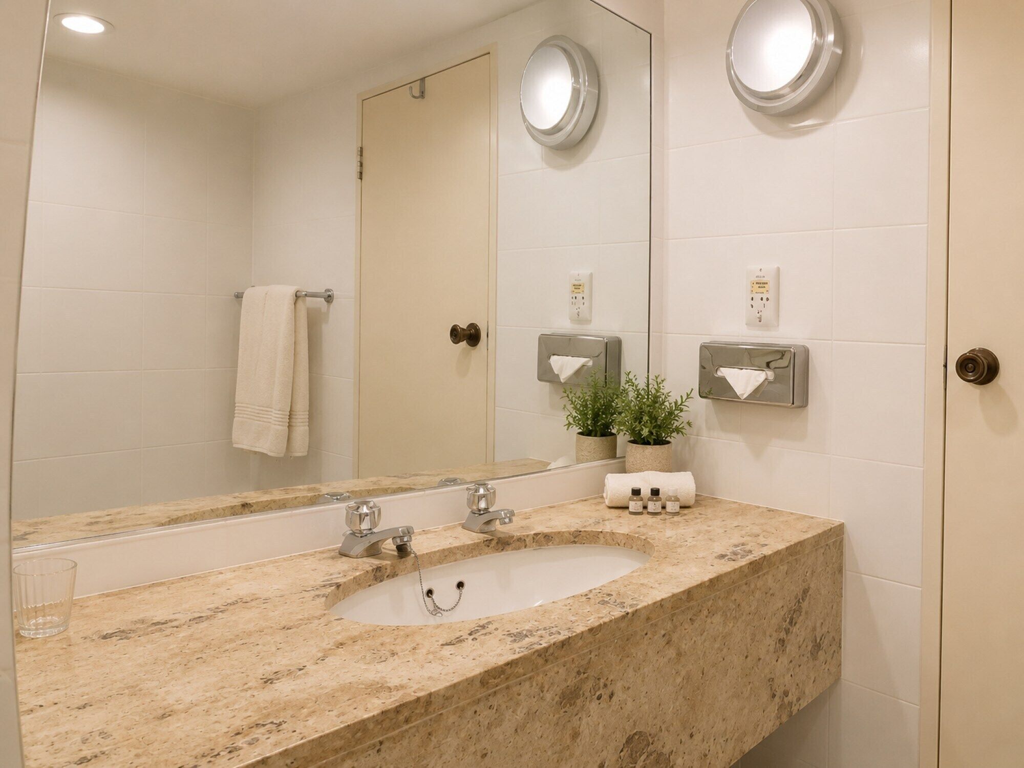 Un baño con lavamanos de mármol, dos espejos redondos, un perchero y una planta en maceta.